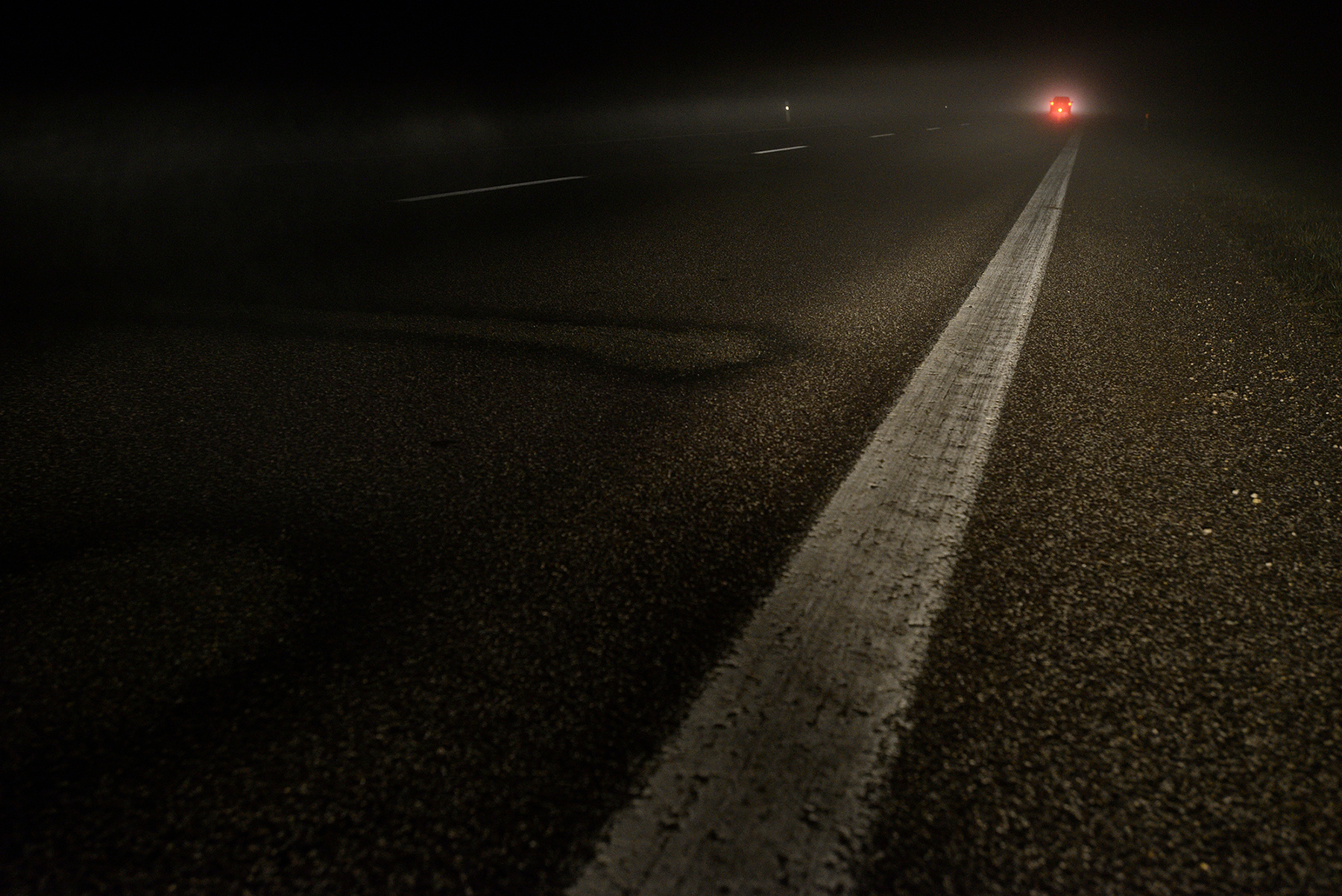 Vanishing car on a nightly foggy road